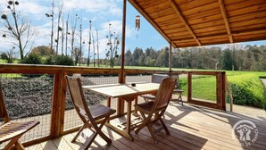 Une terrasse en bois avec une table et des chaises, donnant sur un espace clos planté d’arbres et offrant une vue sur un ciel dégagé.