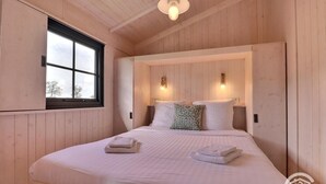 Une chambre à coucher aux murs lambrissés, dotée d’un grand lit, de deux lampes fixées au mur et d’une fenêtre offrant une vue agréable.