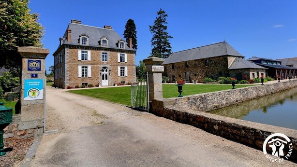Un grand bâtiment en pierre, de style architectural traditionnel, avec une entrée pavée et un élément décoratif aquatique en premier plan.