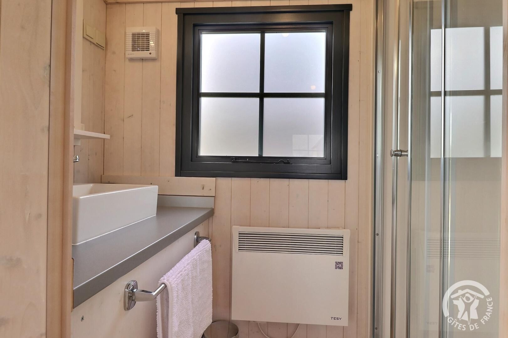 A bathroom with a window, a sink, a towel rack, and a ventilation unit.