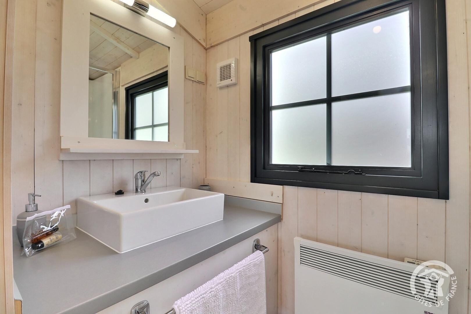 A modern bathroom with a large window, a white sink, and a mirror.