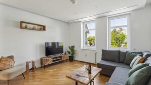 A modern living room with a flat-screen TV, wooden coffee table, grey sofa, and large windows offering a view of greenery. - Cozy apartment in Bad Harzburg with WiFi (Bad Harzburg)