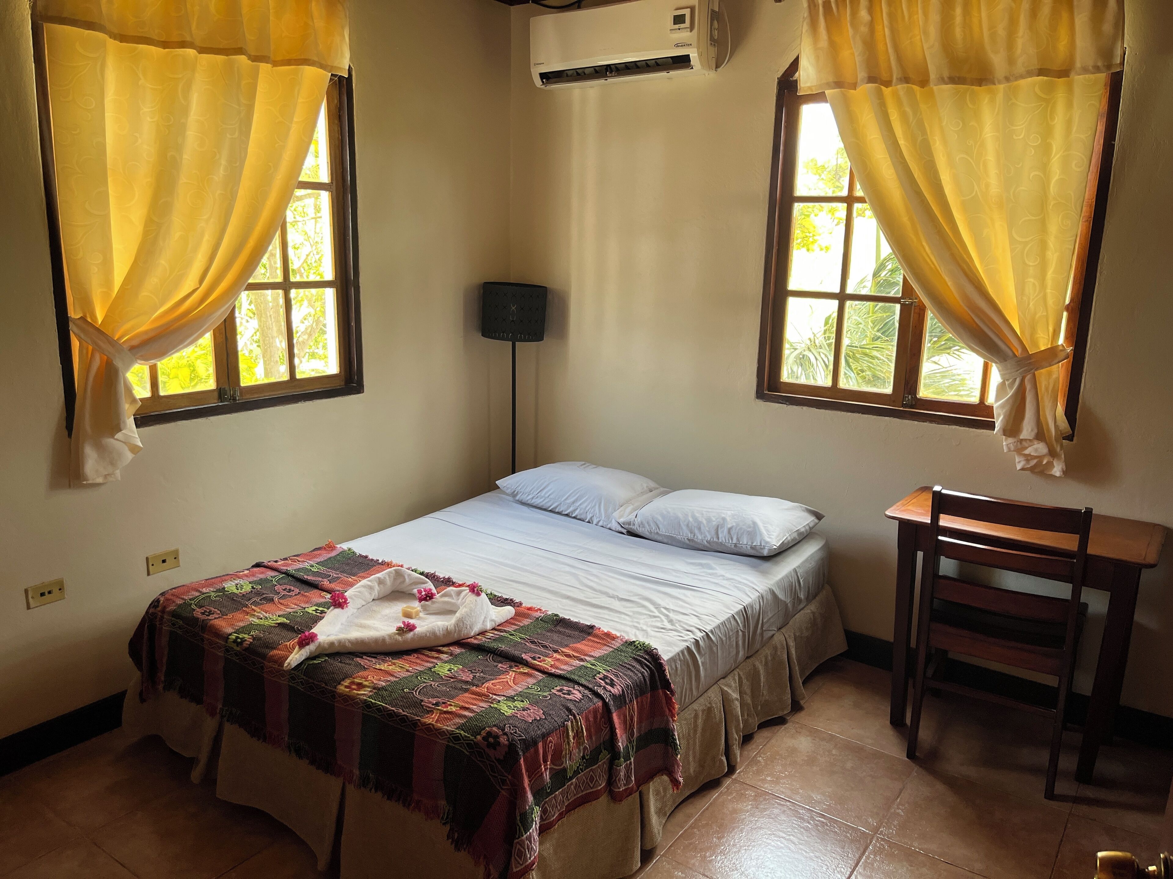 Une chambre à coucher avec un lit, un bureau et deux fenêtres avec des rideaux.