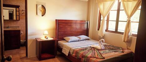 Une chambre avec un lit en bois, une table de chevet avec une lampe, un climatiseur fixé au mur et une fenêtre avec des rideaux.