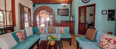 A cozy living room with a wooden ceiling, a sofa set, a coffee table, and a dining area in the background.