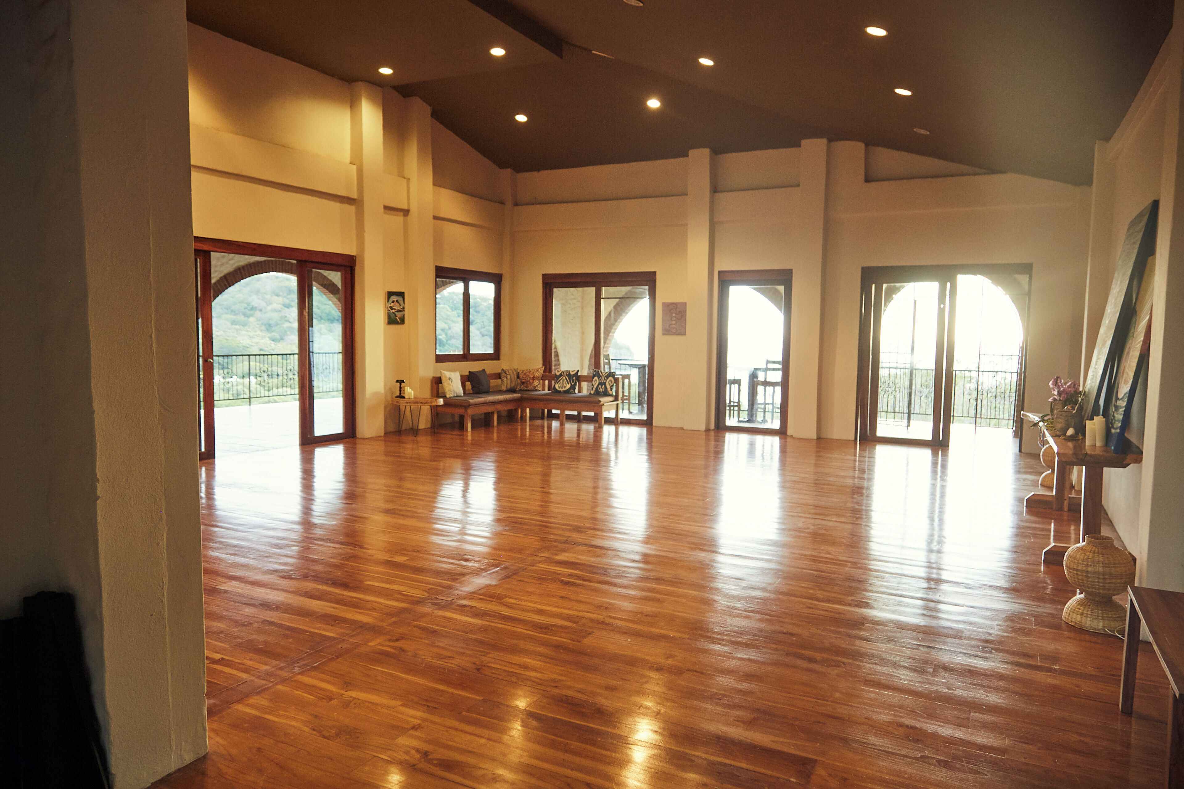 A spacious room with wooden flooring, large windows, and a seating area with a sofa and chairs.