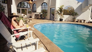 Un espace aménagé au bord de la piscine, avec un bâtiment blanc, une piscine et des chaises longues.