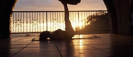 La silhouette d’une personne pratiquant une posture de yoga sous une arche, avec un coucher de soleil en arrière-plan.
