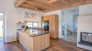 A modern kitchen with wooden cabinetry, a central island, and a glass door leading to a staircase. - Ferienhaus in Kapfenstein (Kapfenstein)