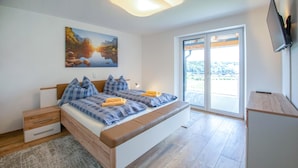 A modern bedroom with a large bed, a desk, and a scenic view through the glass door. - Ferienhaus in Kapfenstein (Kapfenstein)