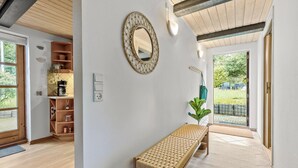 A modern interior with a wooden bench, a wall-mounted mirror, and a kitchen area with a coffee maker. - 2 bedroom pet friendly home in Glesborg (Glesborg)