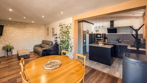 Une cuisine moderne dotée d’un îlot central, un coin repas avec une table et des chaises en bois, et un espace de vie comprenant un canapé et une plante en pot.