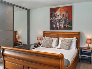 Una habitación de hotel moderna con una cama de madera, dos mesitas de noche con lámparas, un cuadro abstracto grande en la pared y un armario con puerta corredera.