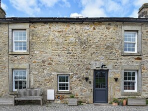 A stone building with two windows and a door, a bench, and a small planter.