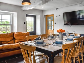 Un coin repas avec une table dressée pour six personnes, entouré de chaises en bois, d’un canapé et d’un téléviseur fixé au mur.