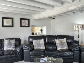 A living room with a black leather sofa set, a glass coffee table with magazines, and framed artwork on the wall.