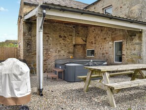 Un bâtiment rustique en pierre, doté d’un patio couvert, d’un jacuzzi et d’une table en bois.