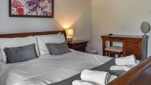 Un letto rifatto con cuscini, una lampada da comodino, un comò in legno con uno specchio e un quadro appeso al muro.