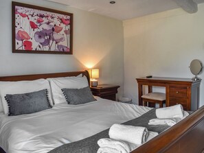 A neatly made bed with pillows, a bedside lamp, a wooden dresser with a mirror, and a painting on the wall.