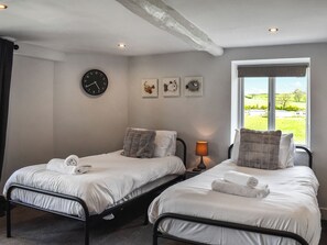 A bedroom with two beds, a wall clock, and a window with a view of the countryside.