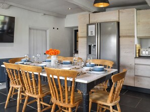 Un comedor con una mesa dispuesta para seis personas, rodeada de sillas de madera. Un jarrón con flores naranjas está sobre la mesa.