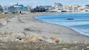 A coastal residential area with houses along the beach, a sandy shoreline, and a clear sky.