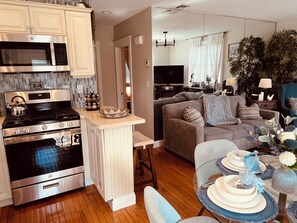 A modern kitchen with stainless steel appliances, a dining area with a round table, and a living room with a sofa and a TV.