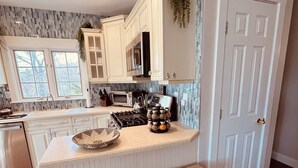 A kitchen with white cabinets, a central island with stools, a microwave, and a sink.