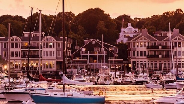 A marina with boats docked, waterfront buildings, and a sunset sky.