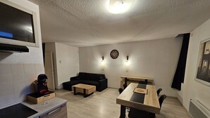 A compact living space with a kitchenette, a sofa, a dining table with chairs, and a clock on the wall.