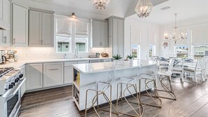 Een moderne keuken met witte kastjes, een groot keukenblok met barkrukken en hanglampen.