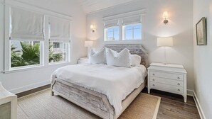 Een slaapkamer met een groot bed, twee nachtkastjes, een plafondventilator en ramen met witte zonwering.