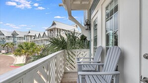 Een houten terras met twee Adirondack-stoelen, een witte balustrade en uitzicht op een rij huizen met puntgevels.