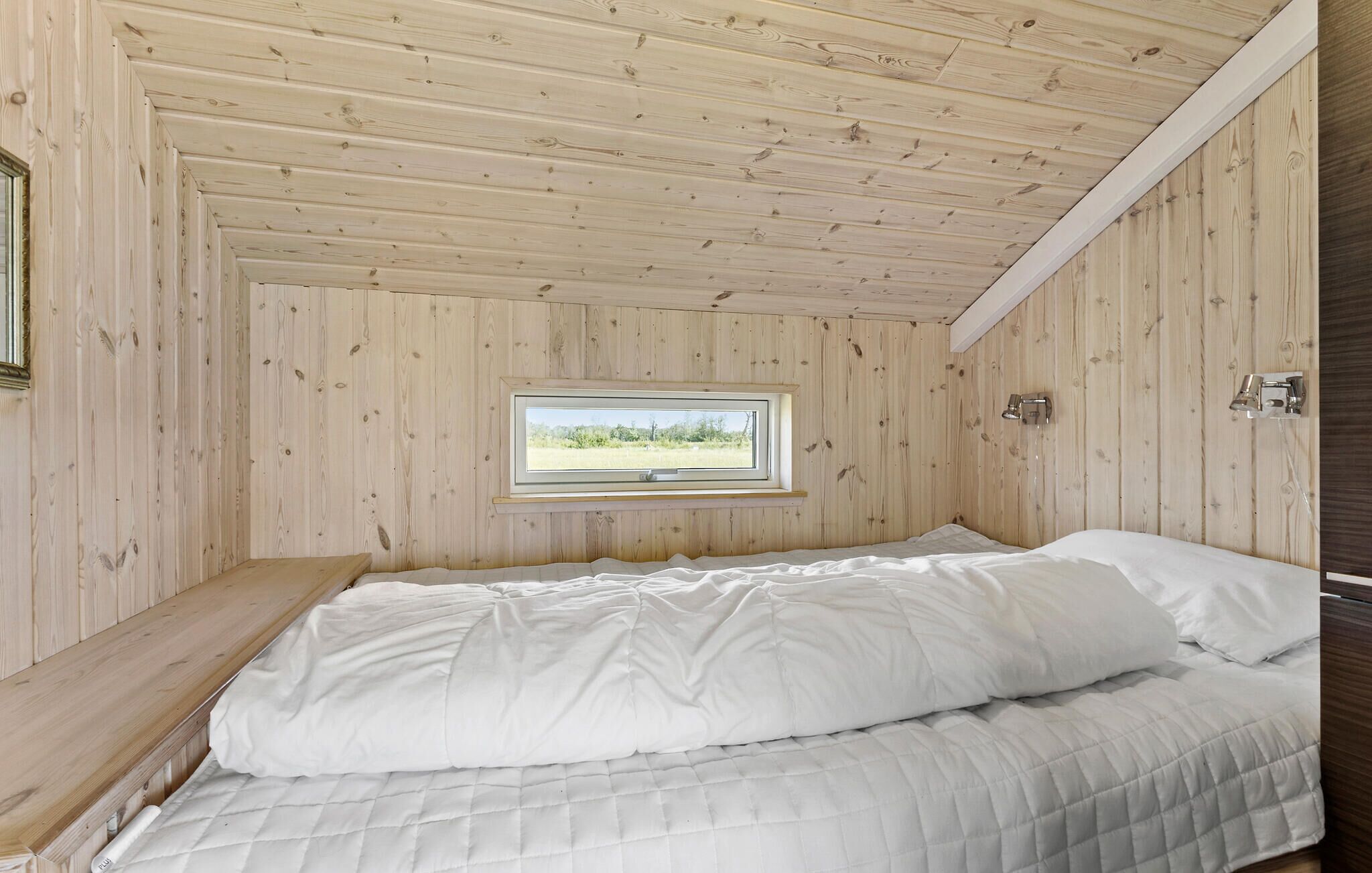 Ein Zimmer mit Holzwänden, einem Bett, einem Fenster und einer Wandleuchte.