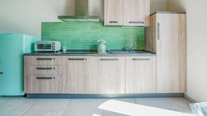 Een keuken met lichte houten kastjes, een groene betegelde spatwand, een inbouwoven en een waterkoker op het aanrecht.
