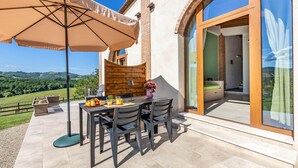 Een terras buiten met een tafel, stoelen en een grote parasol.