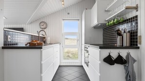 Cocina con armarios blancos, encimera negra, ventana con vistas al exterior y utensilios de cocina colgando.