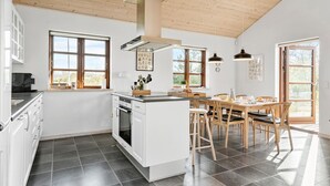 A modern kitchen with white cabinets, a central island, and a dining area with wooden chairs and a table. - Gorgeous home in Ejstrupholm with WiFi (Ejstrupholm)