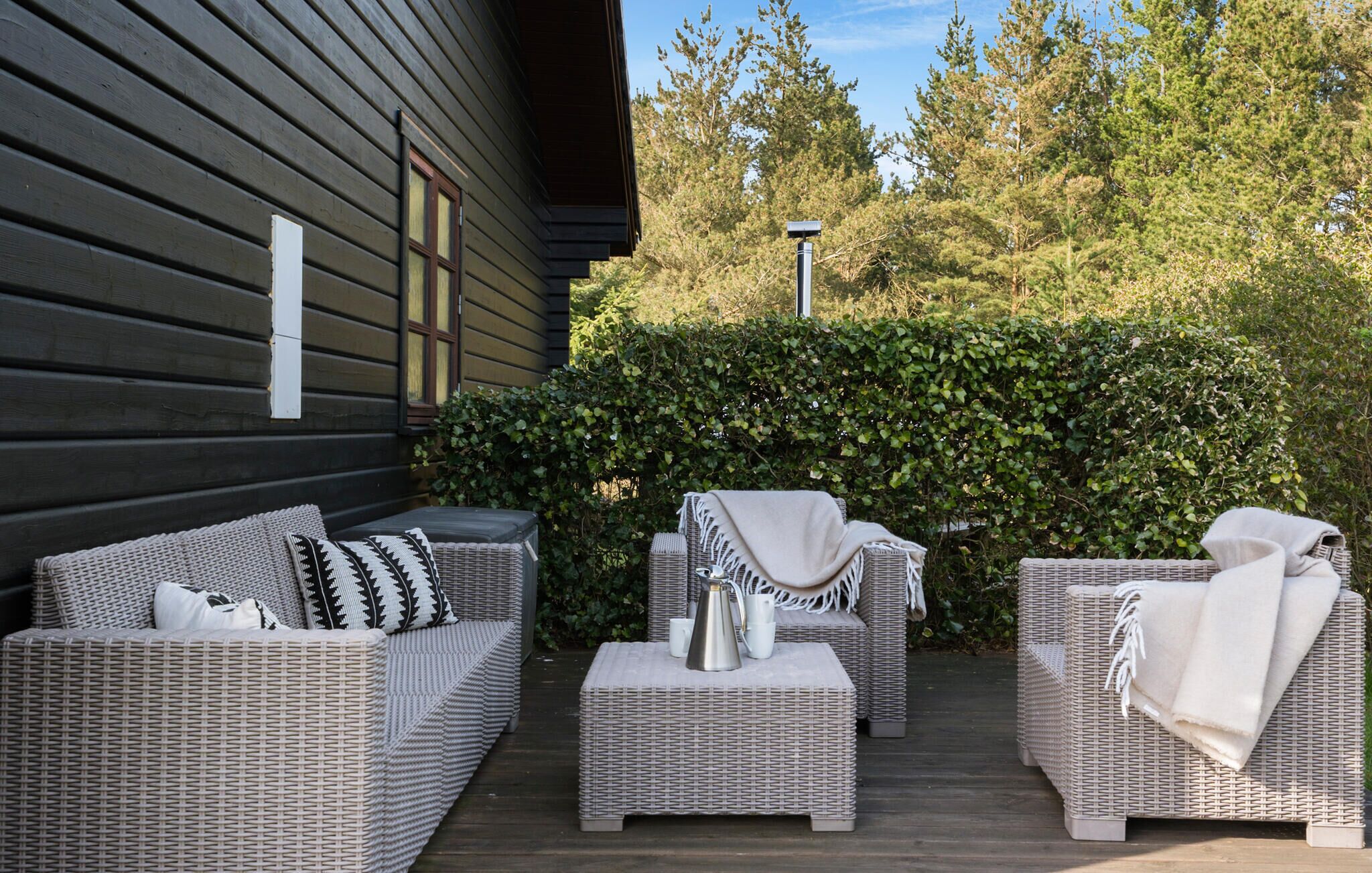 An outdoor seating area with wicker furniture, a coffee table, and a hedge in the background.