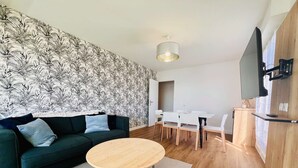 Ein modernes Wohnzimmer mit einem grünen Sofa, einem runden Holztisch und einem wei ßen Esstisch mit Stühlen.