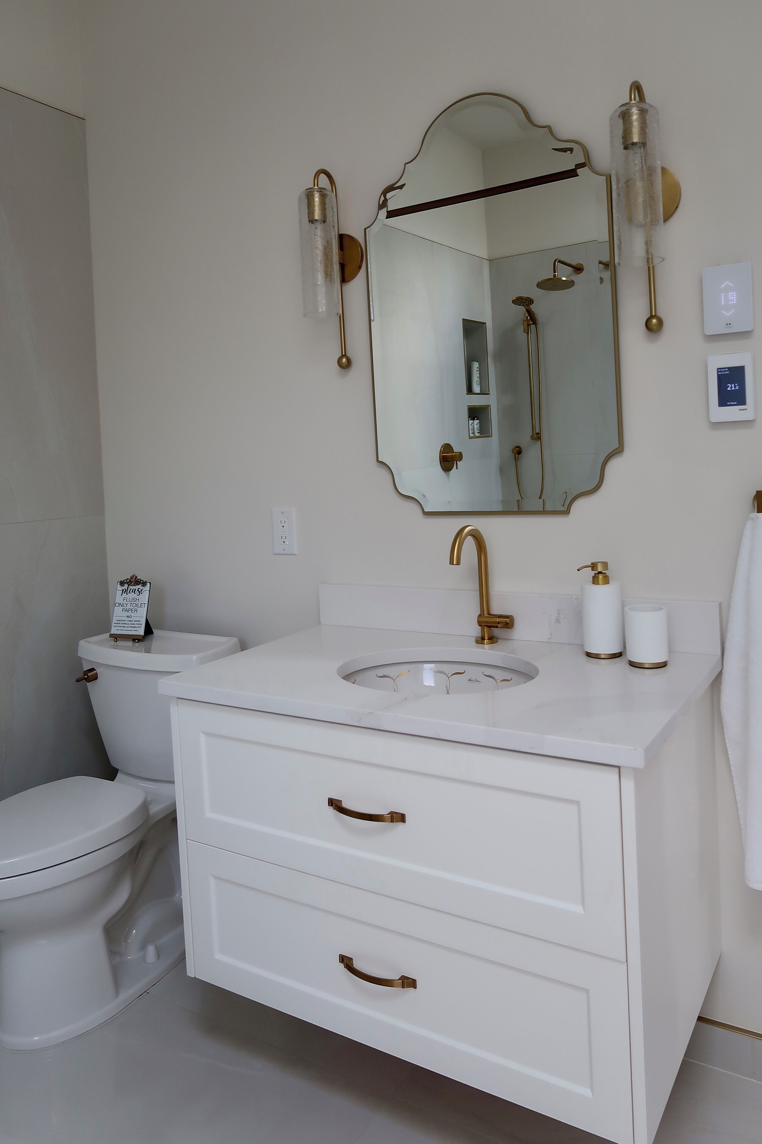 Une salle de bain avec un meuble-lavabo blanc, des robinetteries dorées et un grand miroir.