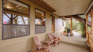 Eine überdachte Veranda mit Adirondack-Stühlen, einem Tisch, einem Grill und einem Briefkasten.