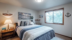 Ein Schlafzimmer mit Bett, Nachttisch, Lampe, Fenster und Wanddekorationen, darunter ein Gemälde und ein Schild.
