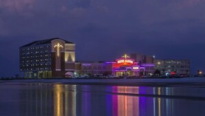 Ein Hotel mit Casino, erkennbar an einer großen, auffälligen Neonreklame, einem mehrstöckigen Gebäude und einem Wasserspiegel im Vordergrund.