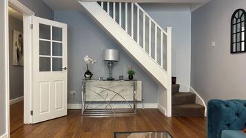 A modern living room with a staircase, wooden flooring, a blue sofa, a white door, and a console table with decorative items.