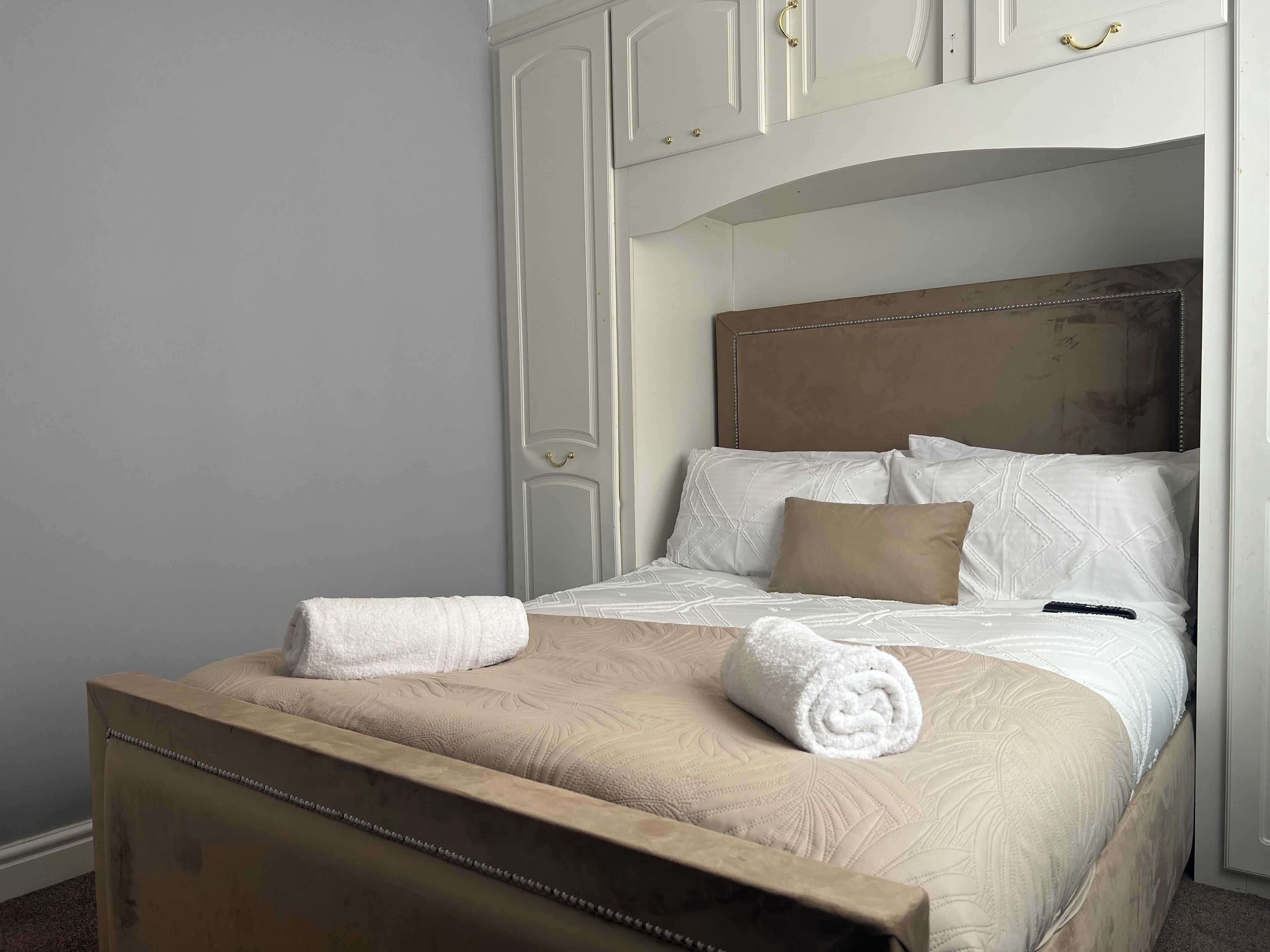 A neatly made bed with a beige headboard and a wooden footboard, accompanied by a matching bench.