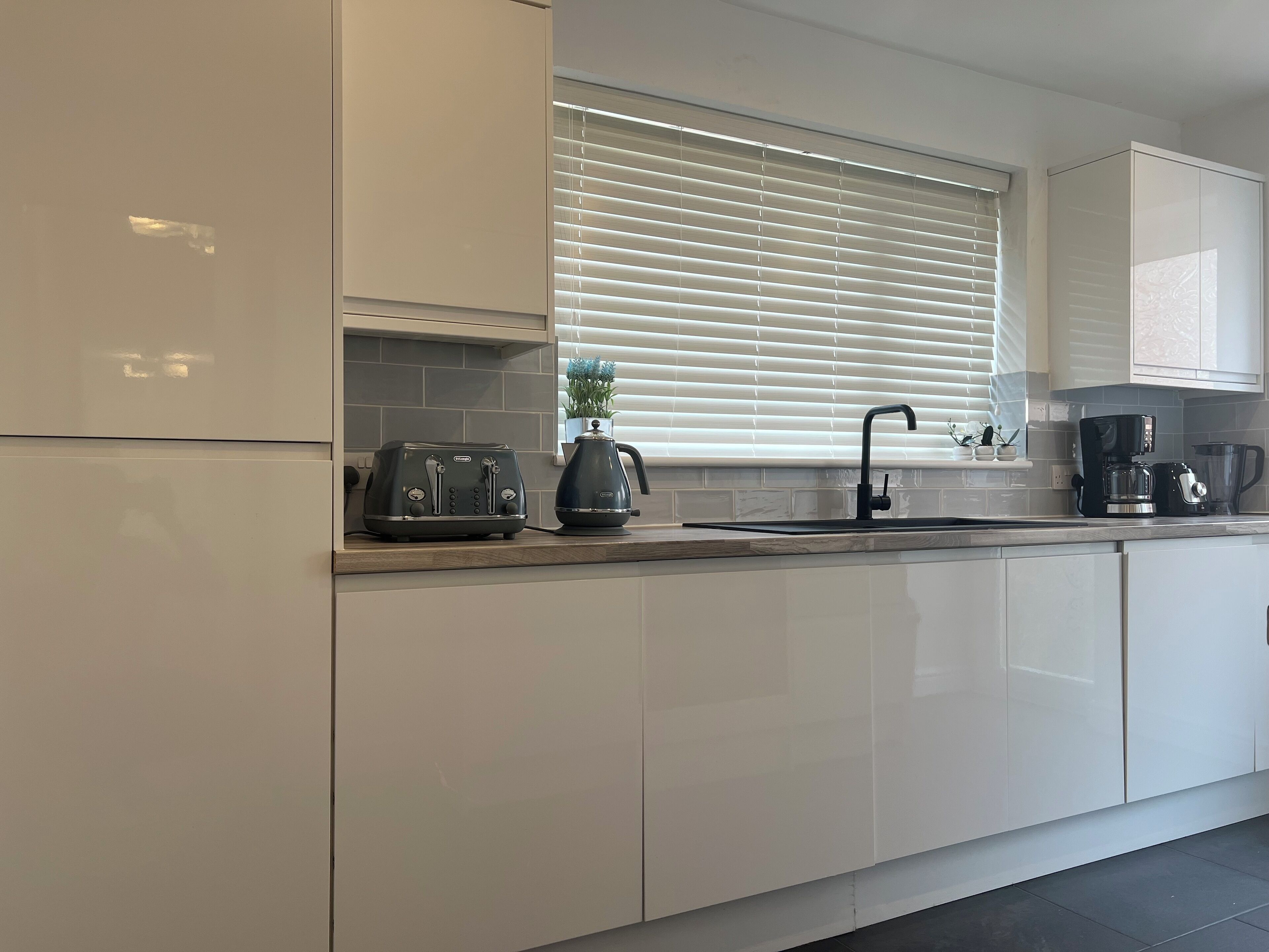 A modern kitchen with white cabinets, a toaster, a kettle, and a coffee maker.