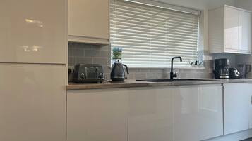 A modern kitchen with white cabinets, a toaster, a kettle, and a coffee maker.
