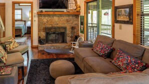 A cozy living room with a stone fireplace, a comfortable sofa, and a television mounted above it. - Serendipity on the river  (Suches)