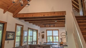 A cozy living room with a wooden ceiling, a sofa with patterned cushions, and a dining area with a table and chairs. - Serendipity on the river  (Suches)